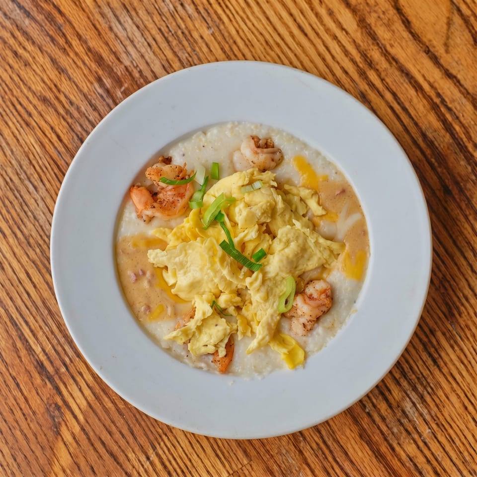 Shrimp and grits with scrambled eggs, cheese, and green onions on a white plate.