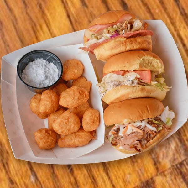 Three sliders with various fillings and a side of fried dough balls with powdered sugar.