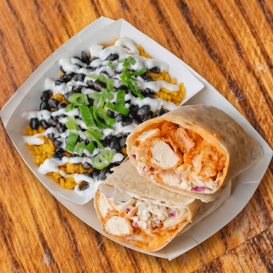 Two chicken wraps with coleslaw and buffalo sauce, alongside yellow rice and black beans.