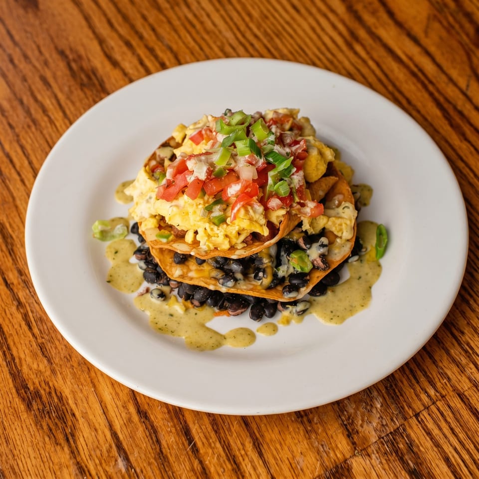 Huevos rancheros with black beans, scrambled eggs, pico de gallo, and green sauce on a white plate.