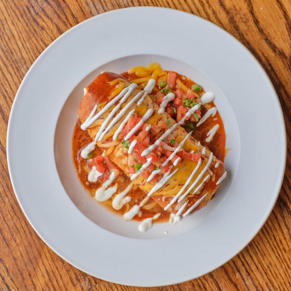 A burrito covered in red sauce, melted cheese, pico de gallo, and a drizzle of sour cream.
