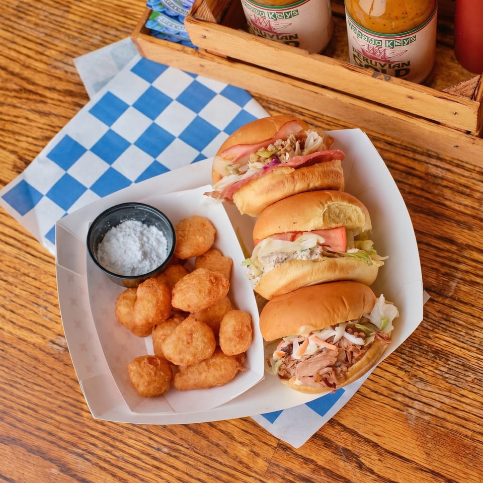Three sliders with various fillings and a side of fried dough balls with powdered sugar.